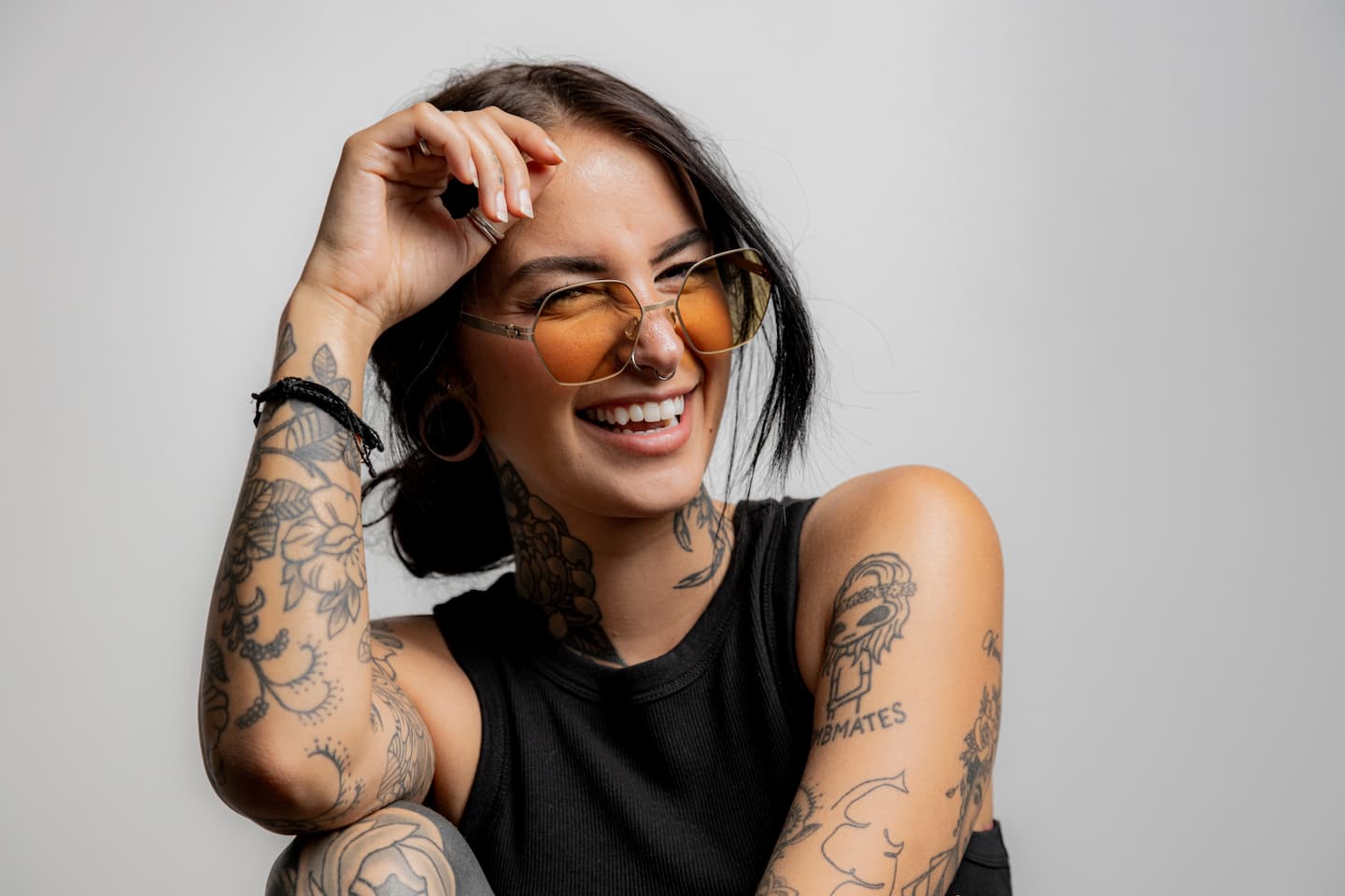 What Is the Best Laser for Tattoo Removal – Smiling tattooed woman wearing sunglasses, showcasing vibrant ink styles, ideal for multi-color laser removal.